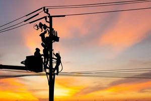 silhueta de eletricista escala um poste e usa um teleférico para manter um sistema de linha de alta tensão, sombra de eletricista eletricista reparador em trabalho de escalada no poste de energia elétrica foto