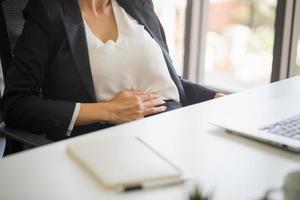 dor de estômago de mulher de escritório insalubre, mulher com dor de estômago se sentindo mal sentada no escritório foto