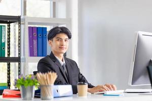 retrato de jovem sorridente sentado em sua mesa no escritório, empresário de terno trabalhando com laptop no escritório foto