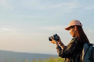 mulheres asiáticas com mochila tirando uma foto à vista no pico da montanha à beira-mar ao nascer do sol