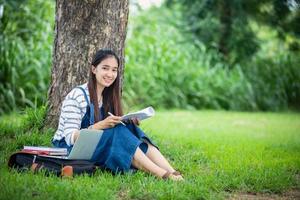 bela estudante asiática segurando livros e sorrindo para a câmera e conceito de aprendizagem e educação no parque no verão para relaxar foto