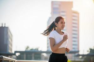 mulher de esporte de fitness jovem asiático correndo e sorrindo na estrada da cidade foto