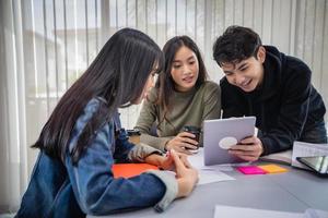 alunos asiáticos do grupo sorriem e lêem o livro e usam o notebook para ajudar a compartilhar ideias no trabalho e no projeto. e também revisar o livro antes do exame foto