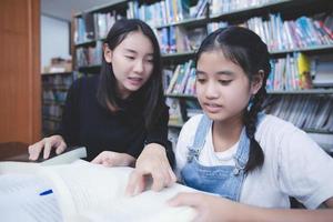 duas estudantes asiáticas lendo livros e usando o notebook na biblioteca. foto