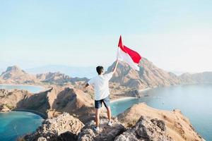 um homem segurando e acenando a bandeira indonésia no topo da montanha em labuan bajo indonésia foto