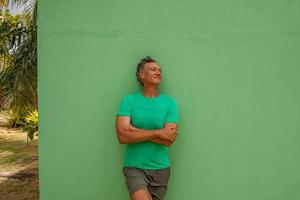 homem maduro relaxando enquanto se encosta em uma parede verde foto