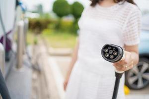 mulher asiática feliz segurando um conector de carregamento dc - ccs tipo 2 ev na estação de carregamento ev, mulher preparando um conector de carregamento ev - veículo elétrico para recarregar um veículo. foto