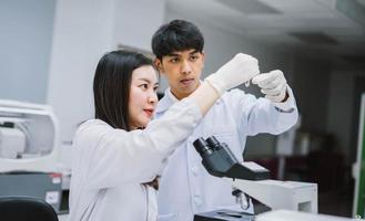 dois jovens cientistas médicos olhando para o tubo de ensaio no laboratório médico, selecione o foco no cientista masculino foto