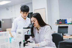 dois cientistas médicos trabalhando em laboratório médico, jovem cientista feminina olhando para o microscópio. selecione o foco na jovem cientista foto