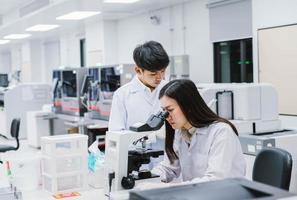 dois cientistas médicos trabalhando em laboratório médico, jovem cientista feminina olhando para o microscópio. selecione o foco na jovem cientista foto