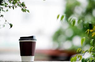 uma xícara de café é colocada nas mãos e no chão com uma rom de cerco verde natural. área comendo café no trabalho caneca de café branca foto