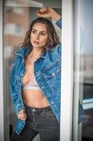 linda mulher morena glamour com jaqueta azul posando na varanda moderna com vista incrível sobre a cidade retrato de uma mulher elegante elegante com cabelo comprido, calça jeans preta vestindo na varanda foto