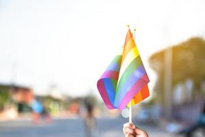 orgulho arco-íris lgbt bandeira gay segurando na mão e sendo acenado na brisa contra o céu azul. foto