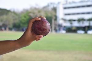 bola de críquete para praticar ou treinar hoiding na mão, fundo de quadra de grama verde turva, conceito para amantes do esporte de críquete em todo o mundo. foto