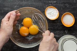 mãos segurando um batedor e tigela com três gemas foto