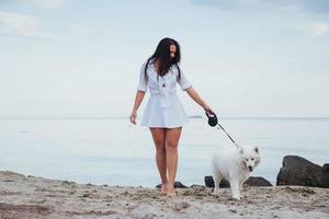 jovem mulher bonita andando com seu cachorro na praia foto