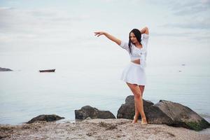 garota de vestido dança com os pés descalços nas mãos da praia de areia foto