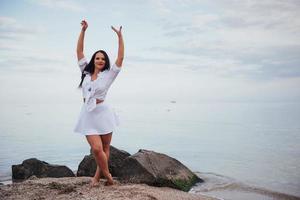 garota de vestido dança com os pés descalços nas mãos da praia de areia foto