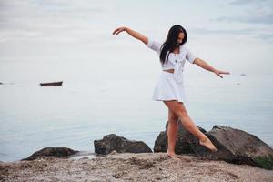 garota de vestido dança com os pés descalços nas mãos da praia de areia foto