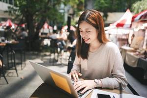 jovem mulher asiática adulta trabalha com computador portátil no café ao ar livre foto