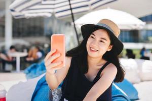 jovem viajante adulto mulher asiática selfie por telefone celular no café de praia ao ar livre no dia. foto