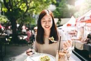 jovem mulher asiática adulta come comida de almoço no restaurante ao ar livre no dia de fim de semana foto