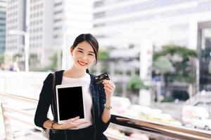 feliz sorriso adulto jovem consumidor de mulher asiática usando cartão de crédito e tablet de tela de maquete para fazer compras. foto