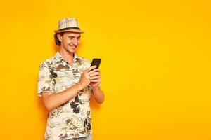 um turista masculino de férias com um smartphone nas mãos escreve uma mensagem e sorri. isolado em um fundo amarelo. espaço para texto. conceito de pessoas, recreação, comunicação em redes sociais foto