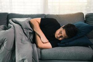 homem asiático sente a doença enquanto estava com frio deitado no sofá e vestindo um cobertor em sua casa.
