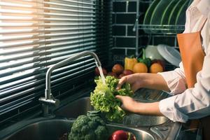 mulher de mãos asiáticas lavando salada de legumes e preparação de alimentos saudáveis na cozinha. foto