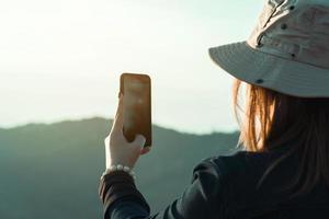 turistas asiáticas usam seus telefones celulares para tirar fotos da paisagem no topo de uma colina fresca.