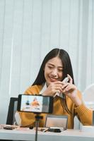 jovem mulher asiática vlogging sobre produtos cosméticos para cuidados com a pele na mesa com sua câmera de vídeo e demonstra o uso do produto e comentários para seu canal de blog online. foto