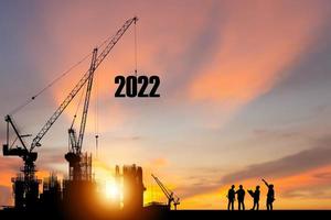 silhueta de trabalhador da construção civil com guindaste e céu pôr do sol para preparação ano novo de 2022 foto