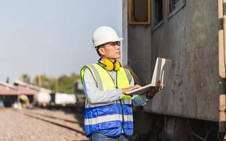 engenheiro homem em coletes e capacetes com laptop em um depósito ferroviário, engenheiro sob inspeção e verificação de processo de construção fábrica de reparação de locomotivas ferroviárias foto