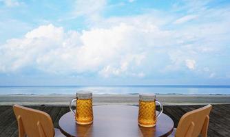 chope ou cerveja artesanal em um copo alto e transparente com espuma de cerveja em cima e há bolhas no copo. cerveja gelada em um copo, colocado em uma mesa de madeira na praia, o mar durante o dia. renderização em 3D foto