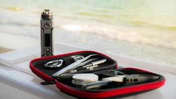 equipamento de manutenção de e-cigarros.consertar ou manter um cigarro eletrônico à beira-mar, sob a luz do sol laranja. foto