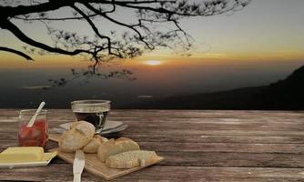 pão caseiro no açougueiro e café preto em vidro transparente para o conceito de café da manhã na mesa de madeira. desfoque de fundo mountian view e nascer do sol. renderização 3D.