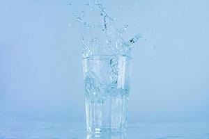 um copo de água espirrou. a água subia de um copo transparente com um quadrado. foto