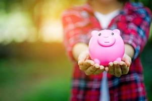 mão feminina segurando o cofrinho rosa, cofrinho e feliz com a economia. e copie o espaço foto