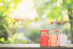 conceito de compras - carrinho de compras ou carrinho, sacolas de compras na mesa de madeira. consumidores de compras on-line podem fazer compras em casa e serviço de entrega. com espaço de cópia foto