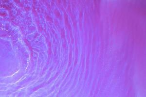 salpicos de água e ondas vista superior com bolhas na luz neon. textura da superfície da água