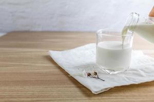 derramando leite saboroso em vidro na mesa de madeira foto