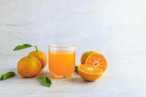 suco de laranja espremido na hora em um copo e frutas cítricas frescas em um fundo branco.