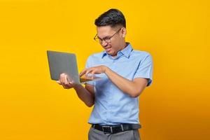 retrato de jovem asiático com raiva asiático em copos usando laptop isolado em fundo amarelo. conceito de empresário e empresário foto