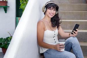 feliz mulher hispânica com bebida para viagem e smartphone ouvindo música foto