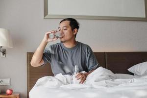 homem sentado na cama e bebendo um copo de água mineral depois de acordar do sono