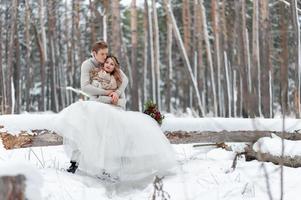 lindo casal apaixonado por um buquê estão sentados no log no fundo da floresta de inverno. obra de arte. casamento de inverno. espaço de cópia foto