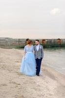 sessão de fotos de casamento de um casal à beira-mar. vestido de noiva azul na noiva.