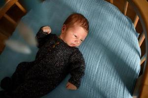 um menino recém-nascido está olhando para a janela em seu berço. um menino nascido com 8 meses de gestação. há um terno de malha no menino. foto