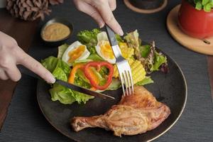 prato de delicioso bife de pernas de frango grelhado com salada de legumes na mesa de madeira foto